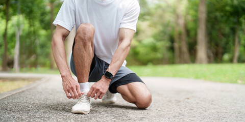 Obraz premium Asian man tying shoelace in park, preparing for outdoor fitness run
