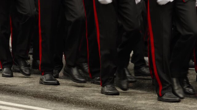 Close-up of uniformed personnel marching in formation on a wet street, highlighting synchronized steps, polished black shoes, and red-striped trousers during a formal parade