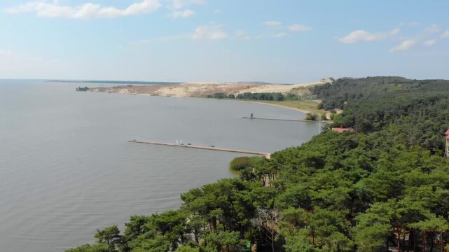 An aerial drone shot captures the stunning natural beauty of the Curonian Spit, a UNESCO World Heritage site in Lithuania. The footage features the vast, rolling sand dunes contrasting with the calm w