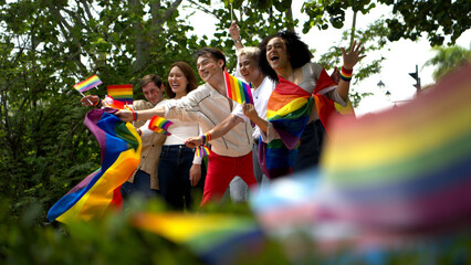 Happy LGBTQ friends running together on a sunny road celebrating pride month, freedom
