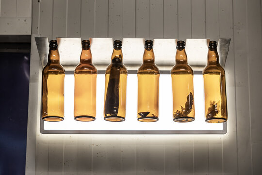 Amber glass beer bottles hanging in front of a bright inspection light inside a brewery, showing residue or samples for quality control, with copy space
