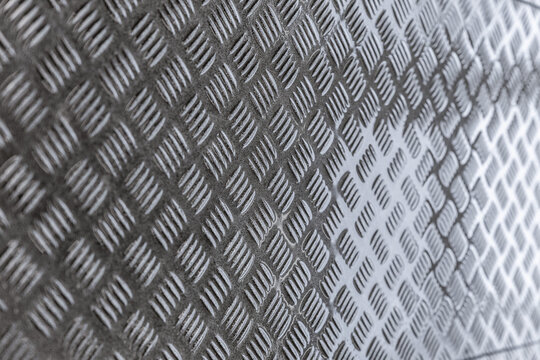 Close-up of gray diamond plate metal surface with raised tread pattern, industrial texture, shallow depth of field, and copy space
