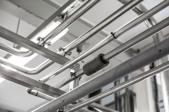 Black and white view of overhead metal pipes, clamps, insulation, and ceiling lights inside an industrial facility