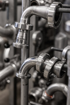 Close-up of stainless steel pipe elbows, threaded fittings, and metal connections inside an industrial processing or manufacturing facility