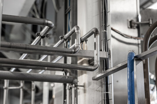 Stainless steel pipes, railings, and structural supports inside an industrial processing facility, with selective focus and copy space