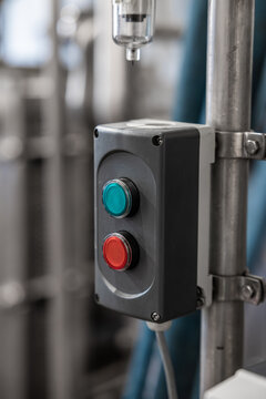 Close-up of red and green control buttons on a gray electrical box mounted beside metal pipes in an industrial facility