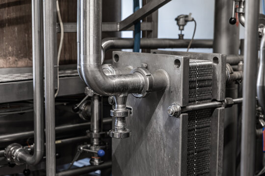 Close-up of stainless steel pipes and a plate heat exchanger in an industrial processing facility, showing valves, fittings, and metal machinery