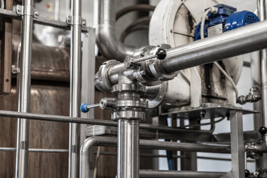 Close-up of stainless steel pipes, valves, tank equipment, and a blue motor inside an industrial processing facility