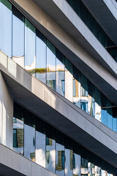 diagonal architecture frames glass windows along an urban building facade, where reflection and perspective reveal balconies between layered exterior bands