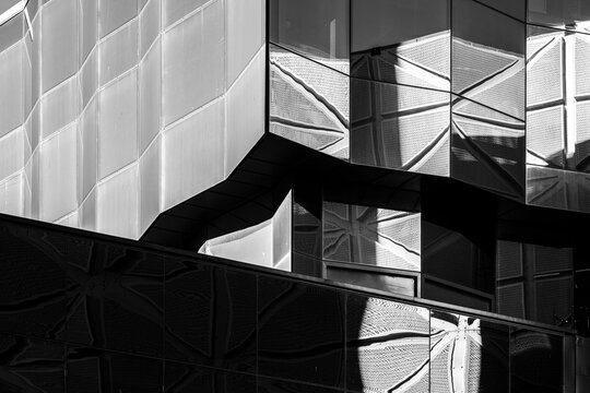 monochrome architecture detail holds angular shadow over a glass building facade, where abstract reflection and contrast sharpen the folded exterior planes