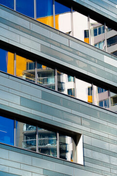 geometric architecture detail frames blue glass windows across an urban building facade, with abstract reflection patterns between metal bands and balconies