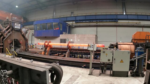 A forging machine processes a red-hot steel ingot in a large steelworks.