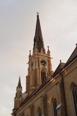 Fototapeta premium Church spire with clock tower, Gothic architecture in brick, ornate rooflines and sunset light on the exterior