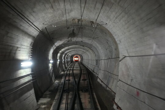 An orange cable car approaching in a dark concrete underground tunnel.