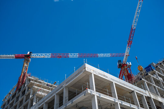 against deep blue sky, construction cranes frame a concrete building site where urban development, city architecture and open floors align
