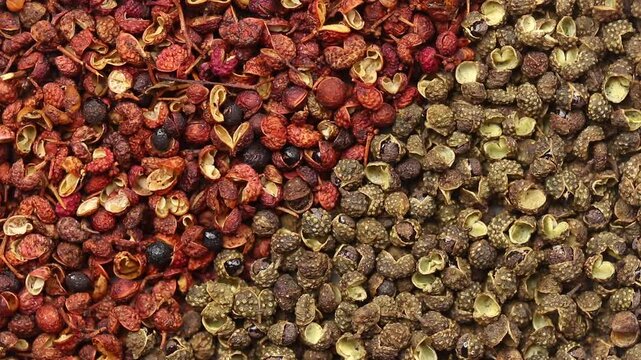 Top view closeup of a slowly rotating pile of red Sichuan peppercorns and green Chinese prickly ash divided into halves.