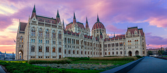 Fototapeta premium Hungarian parliament building on the danube in budapest at sunset, gothic revival spires and ornate facade glowing under a dramatic pink and purple twilight sky