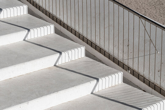concrete stairs run beside metal railing and tiled wall, where urban architecture, shadows and exterior lines emphasize a quiet access detail