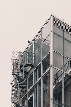 glass building corner rises under pale sky, with metal balconies and exterior stairs tracing urban architecture along a transparent facade