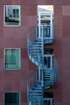 blue spiral stairs curve against red facade and apartment windows, where urban architecture turns exterior access into a graphic building detail