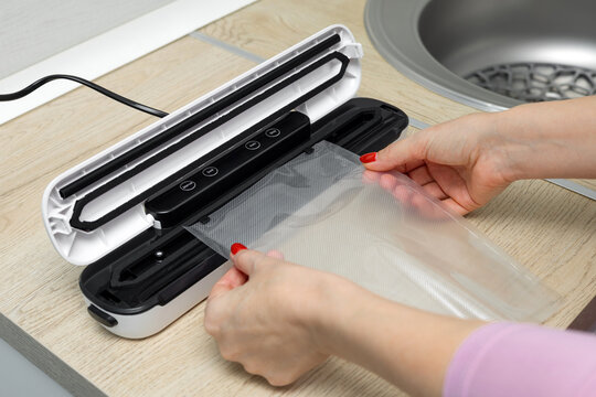 A housewife uses a vacuum sealer for food in the kitchen. vacuum packaging machine. sealing a vacuum sealer bag. 