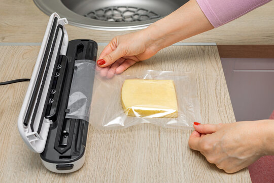 A housewife uses a vacuum sealer for food in the kitchen. packaging of products for long-term storage. vacuum packaging machine. vacuum-packed cheese. 