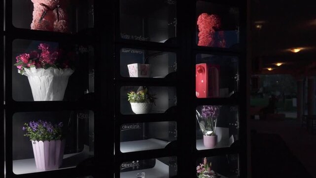 Pink and red rose teddy bear bouquets and potted flowers behind glass of a dispensing machine. Slow motion flower vending machine at night. Innovative and modern 0-24 last minute shopping concept.
