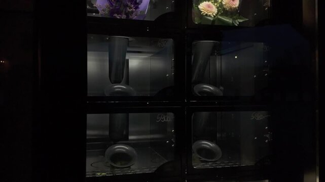 Flower vending machine at night. Bouquets made of fresh colourful flowers behind glass doors of a dispensing machine. Innovative and modern 0-24 last minute shopping concept. Tilt down slow motion.
