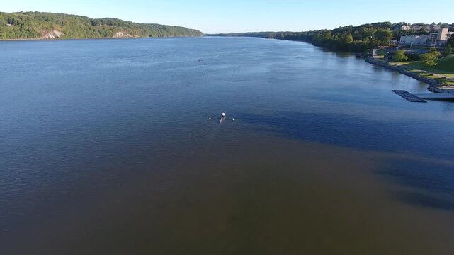 Aerial view of a single rower in a scull boat on the calm Hudson River with forested banks under a clear blue sky, Poughkeepsie, New York, United States.