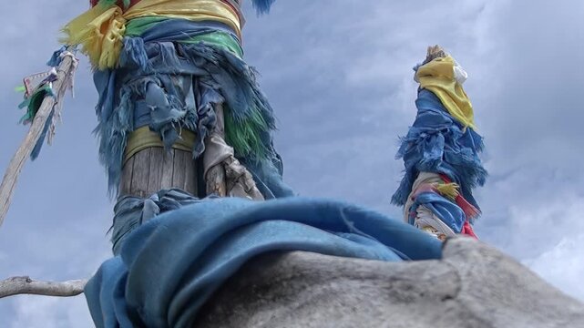 Colorful khadag prayer scarves adorn traditional wooden ovoo shrines, swaying gently against a dynamic sky near the pristine waters of Lake Khuvsgul, Mongolia.