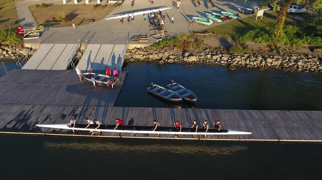 Aerial view of people carrying a rowing shell on a wooden dock at the Hudson River Rowing Association facility during sunset in Poughkeepsie, New York, United States.