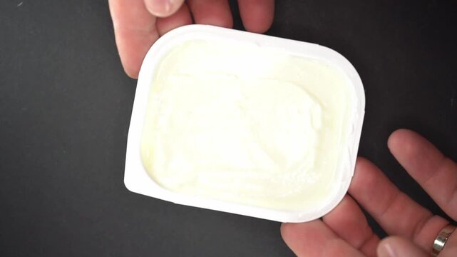 A top-down view of a chef's hands placing a white plastic container of creamy dairy product onto a dark surface, highlighting freshness and preparation.