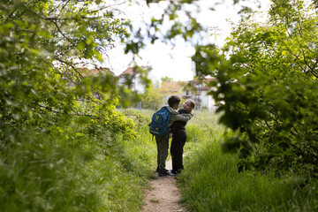 Obraz premium Girl and a boy with school backpack on green path on way home from school. Authentic candid moment of friendship captured on the way home from school on a sunny spring day. 