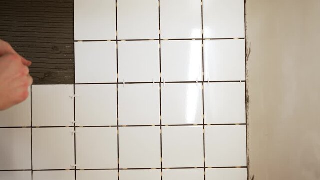Professional construction worker carefully placing white ceramic tiles on a wall, using plastic spacers for precise alignment during a home improvement or renovation project