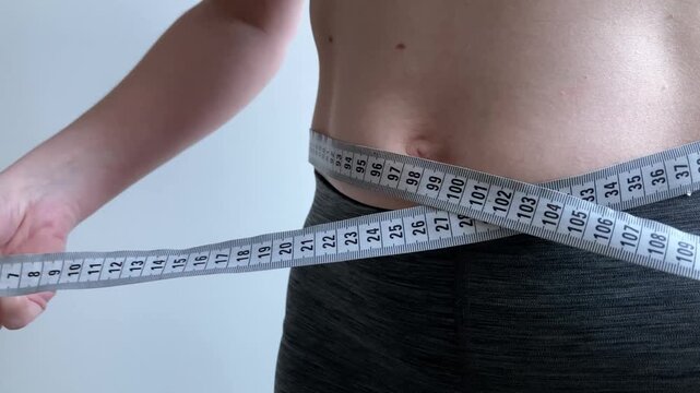 A woman measures the volume of her stomach using a centimeter tape. The moment of the beginning of the summer season and the desire to get rid of excess weight before the warm season. Close-up