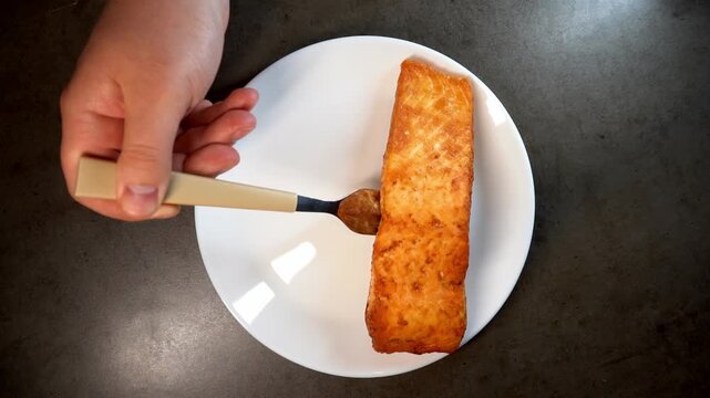 A high-angle close-up of a chef's hands plating a gourmet meal consisting of a seared fish fillet, fresh tomato slices, and a lemon wedge on a clean white plate.