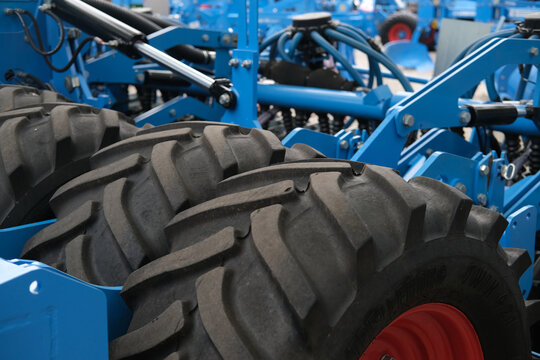 Close view of blue agricultural machinery with large tires, metal frame and hydraulic linkages, ready for field work and cultivation tasks.