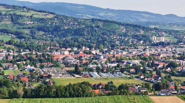 Aerial view of the town of Deutschlandsberg featuring red-roofed houses, green fields, and rolling hills in the background, Deutschlandsberg, Styria, Austria.