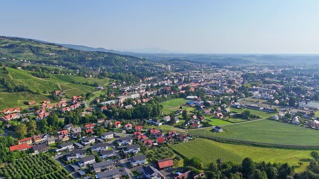 Aerial view of Deutschlandsberg overlooking the town with red-roofed houses, green vineyards, and rolling hills under a clear blue sky in Deutschlandsberg, Styria, Austria.