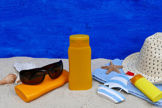 Beach accessories, sunscreen, sunglasses, and a straw hat in the sand.