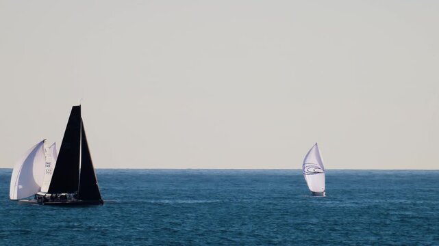 Sailboats participating in competitive regatta race on open sea water during sunny day.