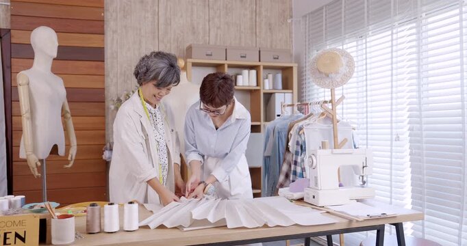 Mother and daughter working together arranging large pleated fabric boutique fashion studio teamwork family business designer sewing pattern making textile entrepreneurship handmade apparel garment