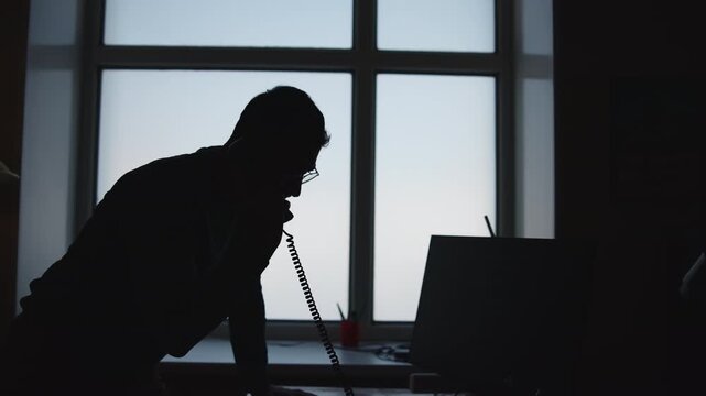 Individual Seated At Windowed Workstation Engrossed In Important Phone Call With Serious Intent. Media