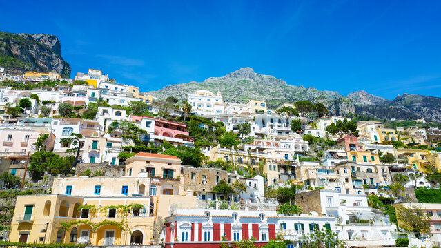 Colorful houses cascaded down steep hillside under clear blue sky in Positano, Italy. Beautiful Italian architecture blends with rocky mountain cliff. Sunny summer day on Amalfi Coast resort 