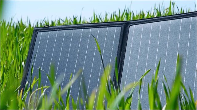 Portable solar panel standing in green grass field outdoors, video of renewable energy technology and eco friendly electricity generation concept