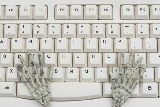Skeleton hands on a white computer keyboard for using old programming languages