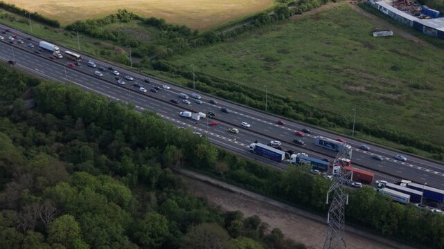 An aerial perspective shows a long line of cars and trucks stopped or moving slowly on a multi-lane highway during the day.