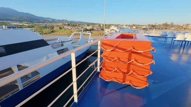 Rows of orange lifeboats on a ferry deck beside a passenger ro-ro vessel in a commercial harbor at sunrise. Shipping safety and tourist travel concepts in Greece, Europe.