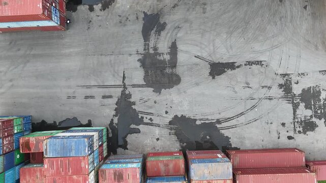 High-angle aerial drone shot of a busy logistics terminal featuring a reach stacker crane moving industrial shipping containers in a large storage yard for global import export trade operations.