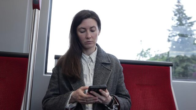 Woman on public transport looking at her phone with trees passing by the window